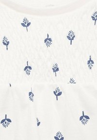 Vit tyg med en texturerad smockdesign som har små marinblå blommönster jämnt fördelade över hela ytan.