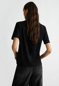 Top nero a maniche corte realizzato in tessuto morbido, con una vestibilità ampia e un design semplice. Cuciture visibili sull'orlo e sulle maniche corte.