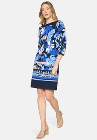 Šaty s květinovým vzorem v modré a námořnické modři, s ¾ rukávy a rovnou siluetou s geometrickým detailem na lemu. Vyrobené z měkké látky.