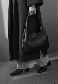 Borsa a tracolla in pelle nera dalla forma arrotondata, con finitura testurizzata e dettaglio con cerniera. Indossata con un cappotto lungo e stivali neri con tacco alto.