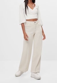 Beige wide-leg jeans made of denim, featuring a classic five-pocket design, visible stitching, and a zip fly with a button closure.