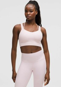 Light pink sports bra with wide straps and a scoop neckline, paired with high-waisted light pink leggings, both in a smooth texture.