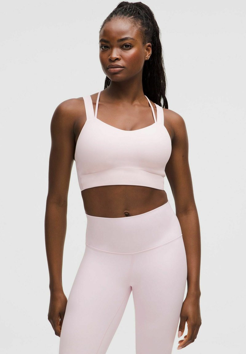 Light pink sports bra with wide straps and a scoop neckline, paired with high-waisted light pink leggings, both in a smooth texture.