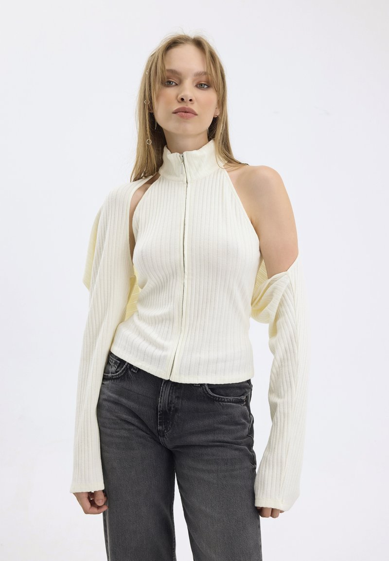 Top a zip con maniche lunghe color giallo chiaro a coste con spalle scoperte, abbinato a jeans grigio scuro.