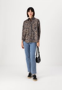 Leopard print shirt in beige and black, paired with light blue straight-leg jeans. Model also carries a small black handbag and wears black sneakers.
