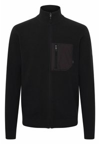 Svart zip-up genser med høy krage, ribbestrikkede mansjetter og nederkant, med en svart stofflomme på brystet med glidelås. Glatt tekstur.