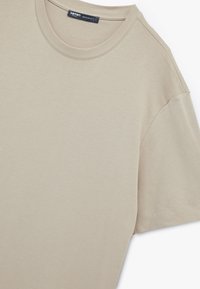 Camiseta de manga corta beige hecha de algodón, con cuello redondo y una textura suave. Ajuste regular con un diseño simple y limpio.