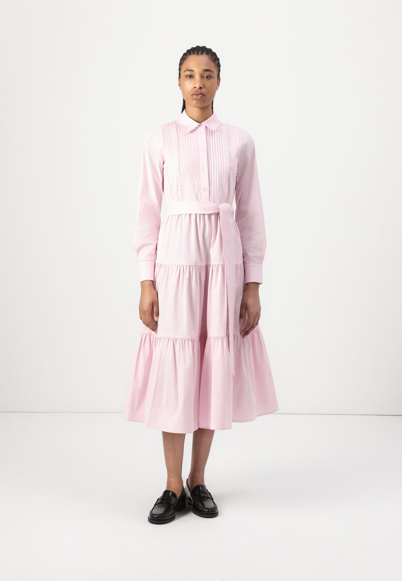Vestido rosa claro feito de algodão, com gola, fecho de botões na frente, mangas longas, saia em camadas e um cinto na cintura para um detalhe adicional.