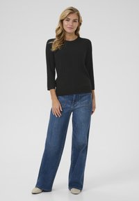 Maglietta nera a maniche lunghe con scollo rotondo, abbinata a jeans in denim blu a gamba larga. L'outfit presenta linee semplici e pulite.