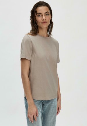 Beige Baumwoll-T-Shirt mit kurzen Ärmeln, rundem Halsausschnitt und entspannter Passform, kombiniert mit hellblauen Jeans. Schlichtes und unauffälliges Design.