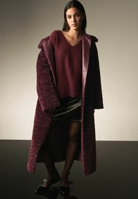 Bordeaux fluffy frakke med satin krave, lagdelt over en bordeaux sweater, parret med en sort lædernederdel og lakerede ankelstiletter.