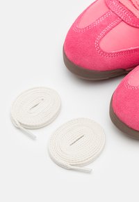 Rosa semskede sko med en avrundet design, med nettdeler og brune gummisåler, ledsaget av to hvite snører.