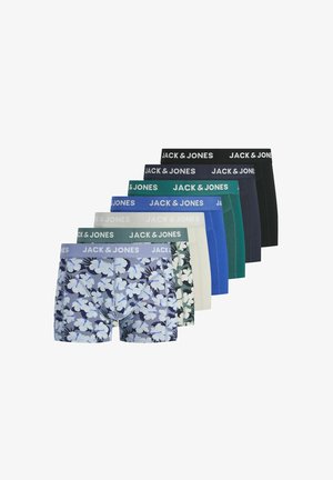 Fiatal férfi göndör hajjal, kék virágmintás boxeralsót visel „JACK & JONES” derékrésszel, egyszínű háttér előtt áll.