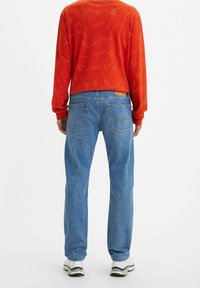 Röd långärmad skjorta med subtilt mönster, kombinerad med blå denimjeans med bakfickor och urtvättad finish. Accentuerad med vita sneakers.