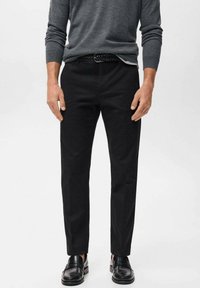 Pantalones negros ajustados de corte recto, confeccionados en tela suave. Combinados con un suéter gris ceñido y mocasines negros.