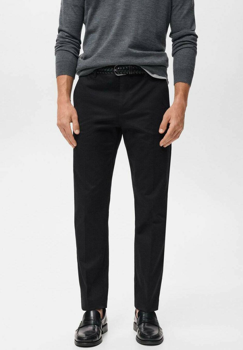 Pantalones negros ajustados de corte recto, confeccionados en tela suave. Combinados con un suéter gris ceñido y mocasines negros.