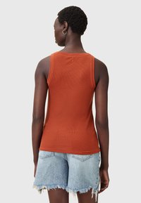 Roestkleurig ribgebreid hemd met brede schouderbanden, gecombineerd met lichtblauwe distress denim shorts met rafelige randen.