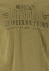 Oliivinvihreä T-paita, jossa on painettu teksti: "MENEMÄSSÄ POIS KOHTI TUNNETTOMAA KOHDETTA, ANNA MATKAN OLLA TUNTEMATON. " Pehmeä ja sileä pinta.