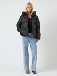 Chaqueta de plumas negra con capucha, que presenta un diseño acolchado y un corte relajado. Combinada con unos vaqueros de pierna ancha de color azul claro y botas de tobillo marrones.
