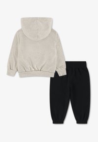 Ανοιχτό μπεζ φούτερ με κουκούλα και κορδόνι, με ριμπ μανσέτες, σε συνδυασμό με μαύρο παντελόνι φόρμας με ελαστική μέση και μανσέτες στα πόδια.