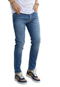 Lichtblauwe denim jeans met een slim fit en vijf zakken. Gecombineerd met meerkleurige sneakers in marineblauw, bruin en crème accenten.