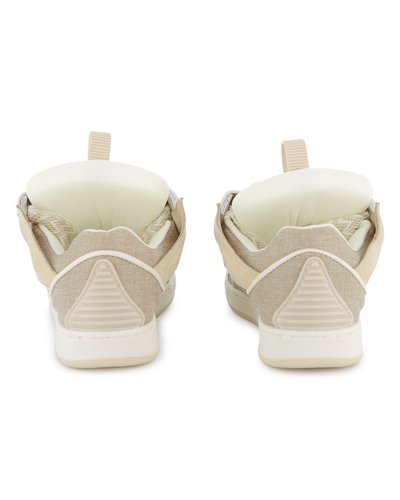 Chaussures de sport beiges avec une tige en tissu texturé, un talon rembourré et des accents blancs. Présentent une languette de tirage à l'arrière et des détails triangulaires sur le talon.