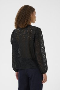 Blusa nera in pizzo con motivo geometrico, maniche lunghe a sbuffo e scollatura rotonda. Tessuto trasparente con dettagli texture.