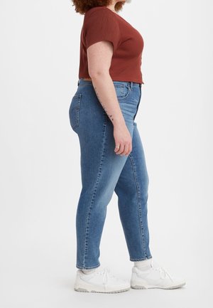 Vaqueros de tiro alto en azul con un ajuste ceñido, que presentan un diseño clásico de cinco bolsillos. Combinados con un top corto de canalé en color óxido y zapatillas blancas.