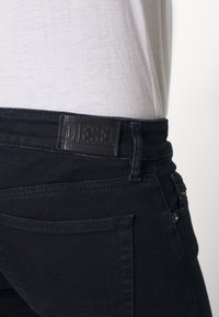 Svarta denimjeans med hög midja, med en texturerad läderlapp märkt "DIESEL" på baksidan, diskret sömnad och ingen synlig slitage.