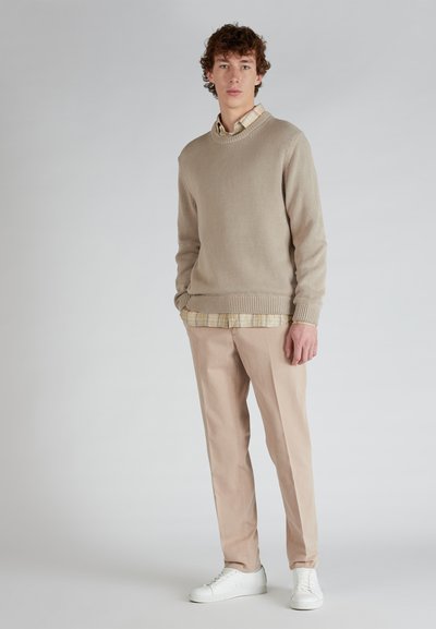 Maglione a maglia beige con orlo a costine sopra una camicia a quadri, abbinato a pantaloni beige chiaro e scarpe da ginnastica bianche. Design semplice e pulito.