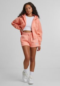 Persikofärgad huvtröja med snörning och framfickor, i kombination med matchande shorts med snörning. Vit crop top och vita sneakers.
