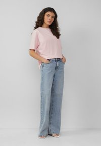 Lichtroze t-shirt met korte mouwen gecombineerd met hoge taille lichtblauwe wijde jeans. De outfit heeft een ontspannen pasvorm en een eenvoudig ontwerp.