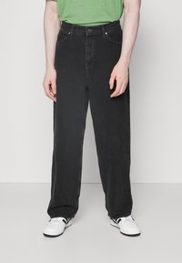 Černé džíny rovného střihu s knoflíkovým zapínáním, dvěma předními kapsami a jemným prošíváním na švech, doplněné bílými teniskami.