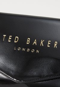 Black textured synthetic clutch with a gold-toned embossed logo reading "TED BAKER LONDON" on the front. Compact rectangular shape.