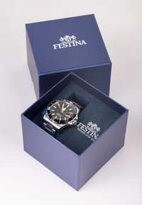 Festina sat u plavoj kutiji, s metalnom srebrnom narukvicom, crnim brojčanikom i bijelim detaljima. Kutija ima mekani unutrašnji dio i utisnutu oznaku.