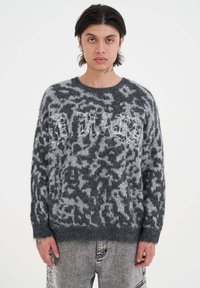 Grijze gebreide trui met een fuzzy textuur, voorzien van een zacht dierenprint en contrasterende witte tekst "HARD" over de borst. Relaxte pasvorm.