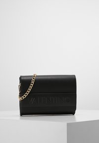 Borsa a tracolla in pelle nera con catena dorata, caratterizzata da un logo in rilievo sulla parte anteriore e una forma rettangolare strutturata.