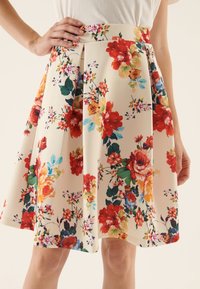 Blommig kjol i krämfärgad tyg, med röda, orange och blå blommor, plisserad design och en figurnära midja. Slät textur.