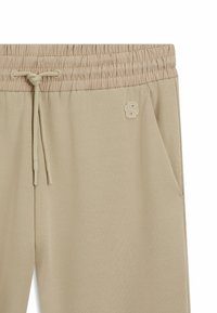Beiga sweatpants har en smockad midja med dragsko, sidficka och broderad logotypdetalj på framsidan.