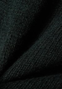 Gros plan sur un tissu tricoté vert foncé montrant des fils texturés détaillés et un motif de point côtes.