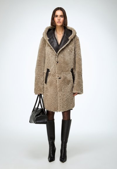 Palton bej cu textură, blană, cu glugă mare, accente din piele neagră, două buzunare frontale și nasturi, asortat cu cizme negre până la genunchi.