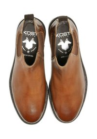 Chaussures en cuir marron avec des panneaux élastiques sur les côtés, bout rond et semelle foncée contrastante. La doublure intérieure présente un logo de la marque en noir et blanc.