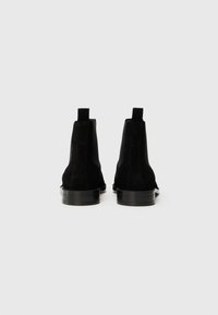 Bottines en daim noir avec une finition lisse, des panneaux latéraux en élastique et une semelle plate en caoutchouc noir. Talon renforcé pour un meilleur soutien.