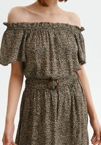 Brun off-shoulder topp med abstrakt creamfärgad mönster, elastisk halsringning och strukturerad midja med en rund brun spänne.