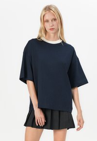Námornícka oversize tričko s krémovým rebrovaným okrajom na krku. Tkanina sa zdá byť mäkká, hladká na dotyk, krátke rukávy a pohodlný strih.