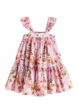 Enfant debout sur une plage portant une robe rose sans manches avec des bretelles froufroutantes et un motif floral.