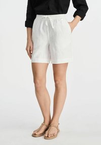 Białe lniane szorty z elastycznym pasem, sznurkiem i bocznymi kieszeniami. Płaskie wykończenie i gładka tekstura. W połączeniu z beżowymi sandałami.