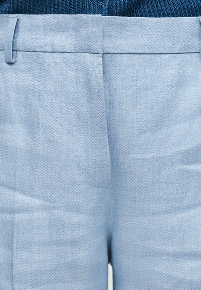 Λεπτομέρεια της μέσης και του μπροστινού πέτασμα ελαφρώς γαλάζιου λινών παντελονιών πάνω σε σκούρο μπλε πλεκτό τοπ.