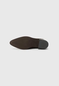 Semelle de chaussure en cuir marron avec une forme pointue. Présente une surface texturée et un talon gris contrastant. Branding minimal visible.