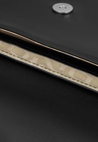 Clutch in pelle nera con chiusura metallica a scatto e fodera interna a motivo beige ben visibile lungo il bordo.